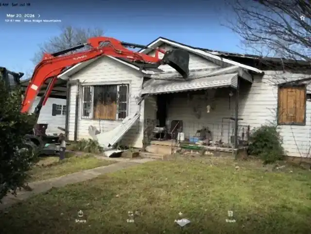 Excavator working beside a small house during demolition