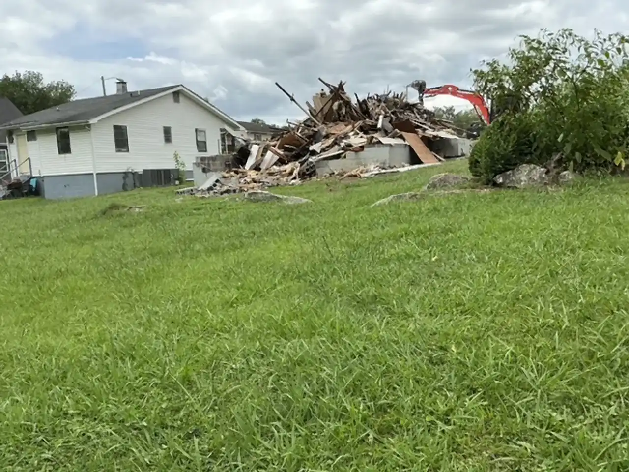 Wide view of a house teardown in progress with the excavator working the debris pile, R&G Land Clearing