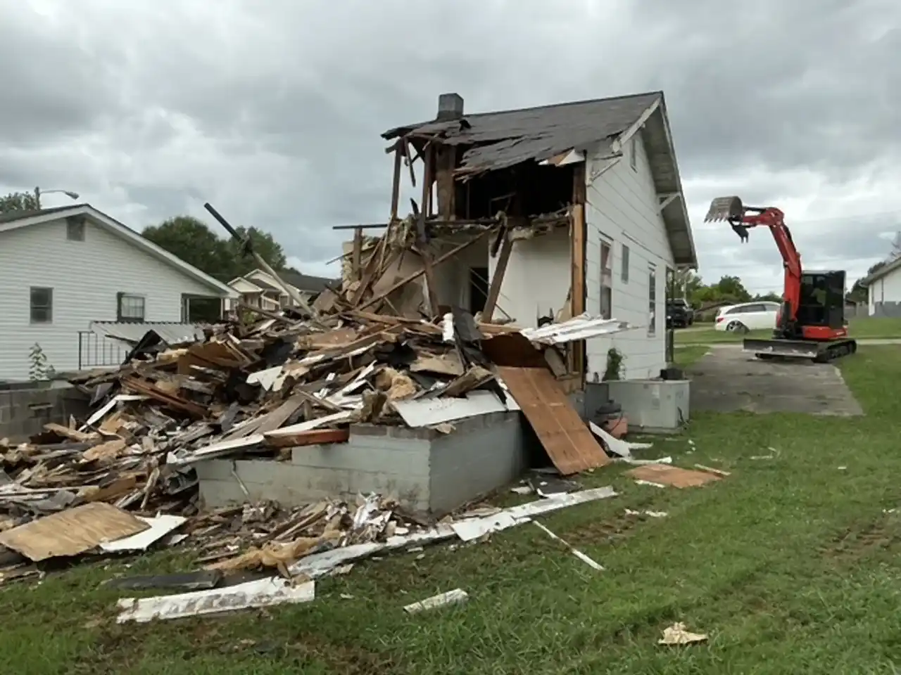 House half torn down with framing and debris exposed, excavator working behind, R&G Land Clearing