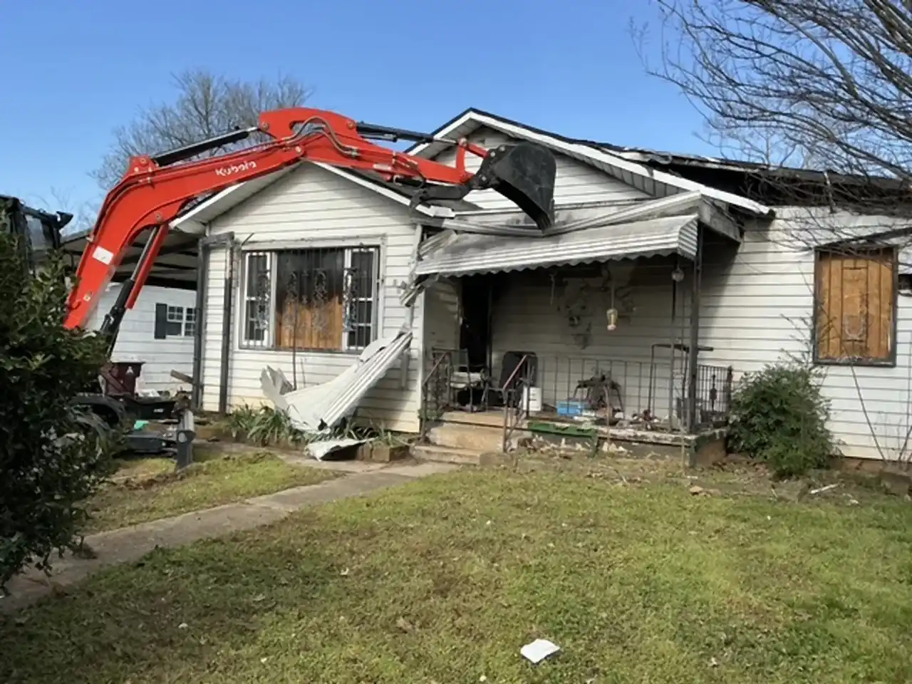 Excavator pulling the porch roof off a damaged house at the start of demolition, R&G Land Clearing