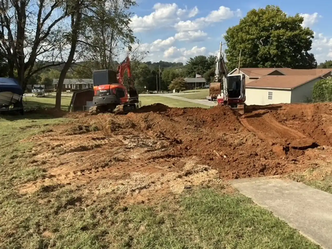 Two excavators backfilling a removed pool with red clay, R&G Land Clearing
